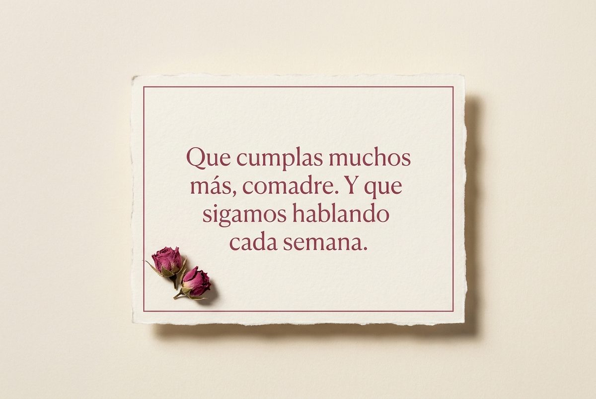 Tarjeta de cumpleaños de papel crema hecho a mano, con borde deckle y un filete impreso en rosa oscuro, fotografiada en plano cenital. En la tarjeta se lee «Que cumplas muchos más, comadre. Y que sigamos hablando cada semana.». Al lado, dos capullos de rosa secos en la esquina inferior izquierda.