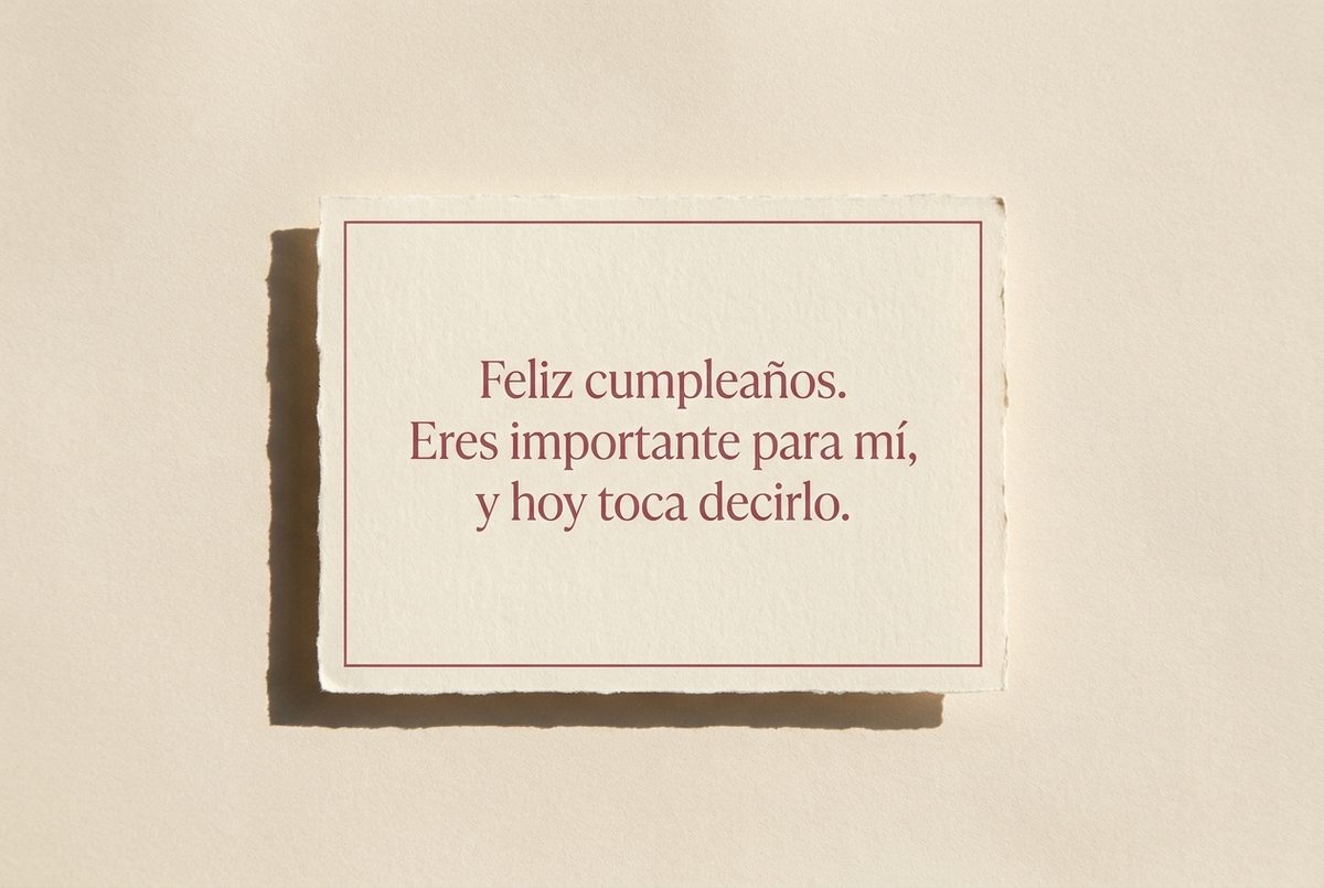 Tarjeta de cumpleaños de papel crema hecho a mano, con borde deckle y un filete impreso en rosa oscuro, fotografiada en plano cenital. En la tarjeta se lee «Feliz cumpleaños. Eres importante para mí, y hoy toca decirlo.». Al lado, la tarjeta sola, con una sombra suave en diagonal.