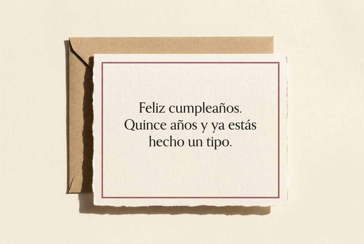 Tarjeta de cumpleaños de papel crema hecho a mano, con borde deckle y un filete impreso en rosa oscuro, fotografiada en plano cenital. En la tarjeta se lee «Feliz cumpleaños. Quince años y ya estás hecho un tipo.». Al lado, un sobre de papel kraft detrás, por el lado izquierdo.